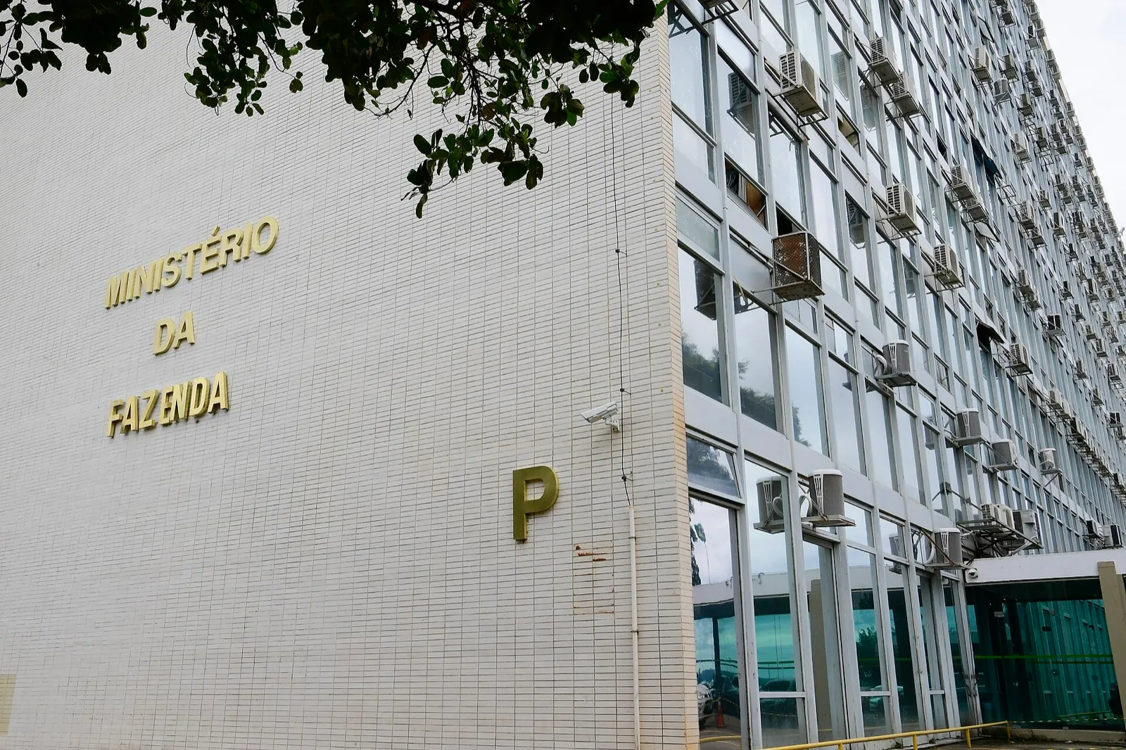 Fachada do prédio do Ministério da Fazenda, com o nome do ministério e a letra P em dourado na parede branca, ao lado de janelas com aparelhos de ar-condicionado.