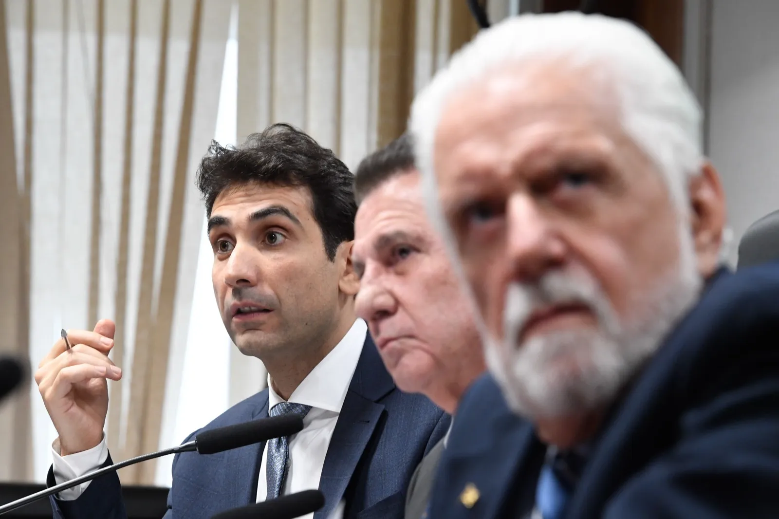 Gabriel Galípolo fala ao microfone durante sabatina no Senado, com dois senadores sentados ao lado