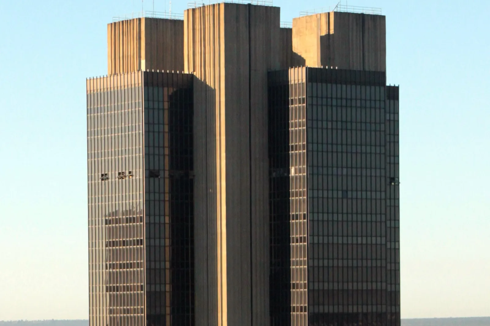Fachada da sede do Banco Central do Brasil em Brasília, torre de concreto e vidro escuro sob céu azul.