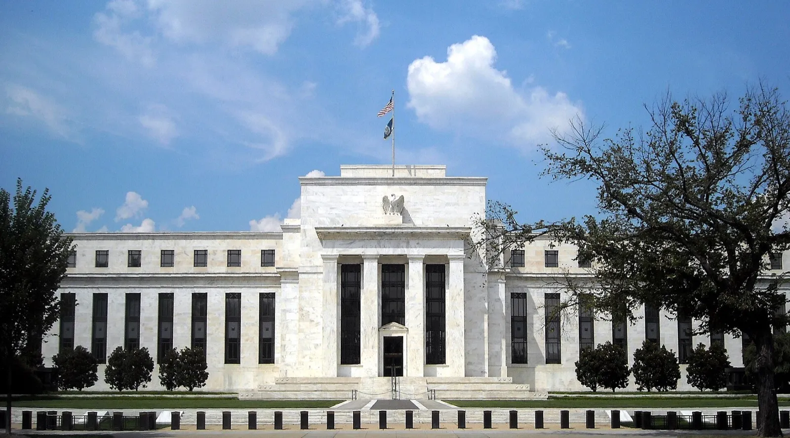 Edifício-sede do Federal Reserve visto de frente, com colunas e bandeira dos Estados Unidos