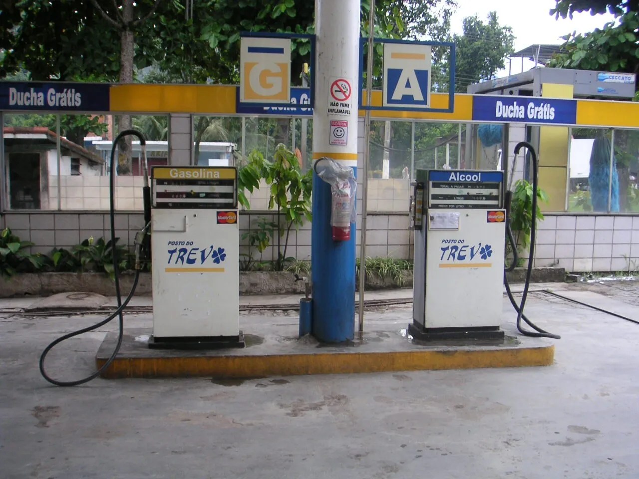 Duas bombas de combustível de um posto no Brasil, com as indicações Gasolina e Álcool, cartões de crédito e uma coluna azul ao centro.