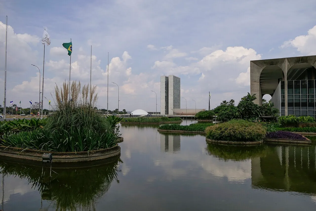 Espelho d'água com canteiros em Brasília, com as duas torres do Congresso Nacional ao fundo e um prédio de colunas de concreto à direita.