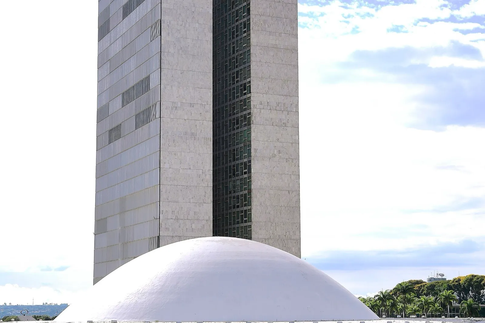 Fachada do Palácio do Congresso Nacional, em Brasília, com a cúpula branca em primeiro plano, as duas torres ao fundo e o espelho d'água na base do prédio.