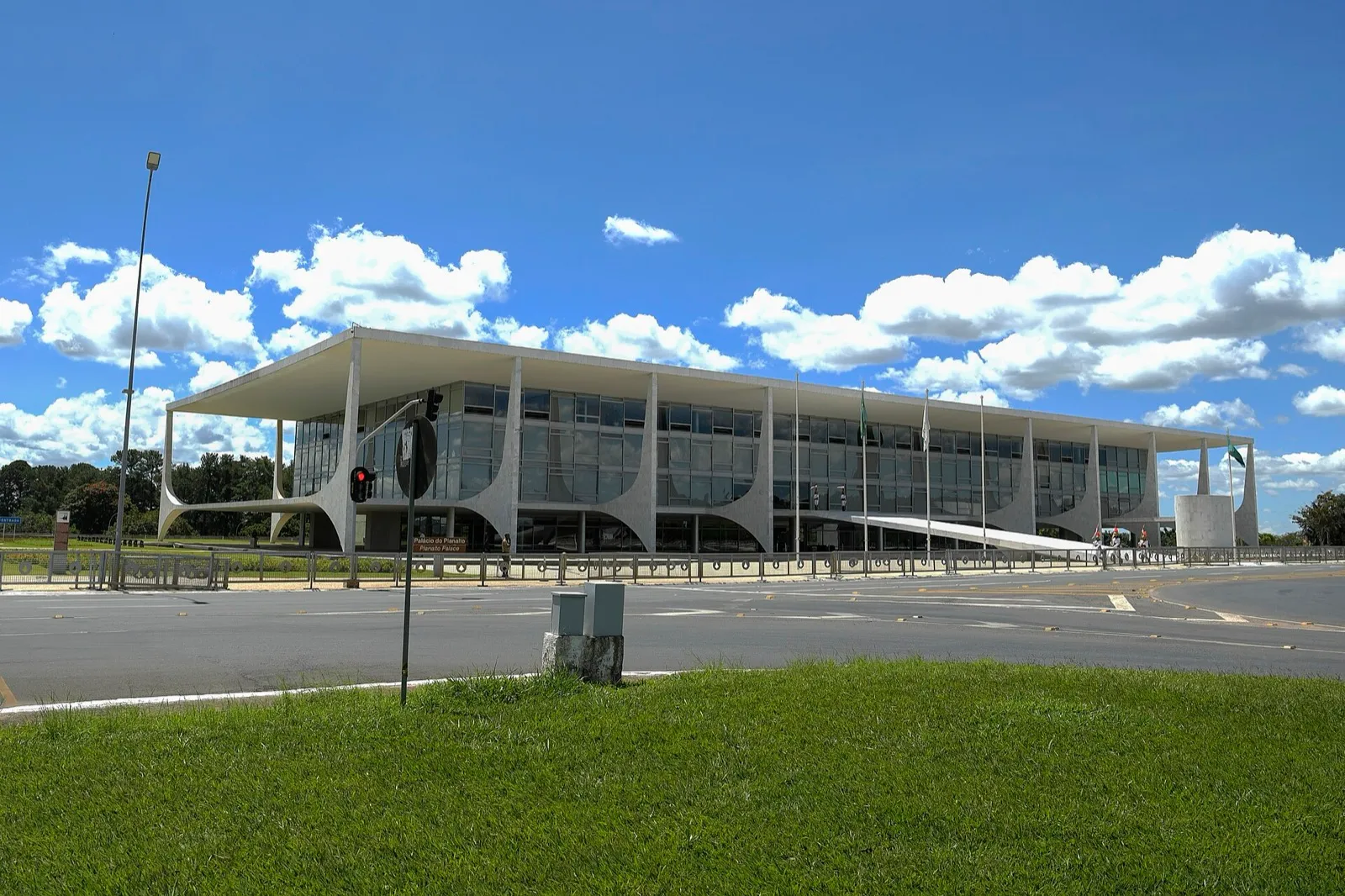 Fachada do Palácio do Planalto, em Brasília, com colunas brancas curvas e vidraças, sob céu azul com nuvens.