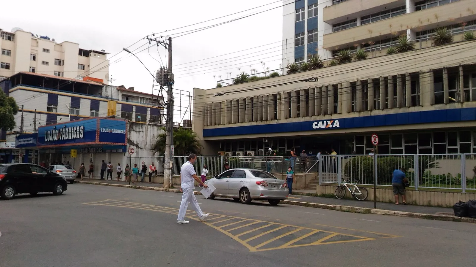 Fila de pessoas em frente a uma agência da Caixa em Viçosa, Minas Gerais, com prédio de fachada azul e letreiro CAIXA.