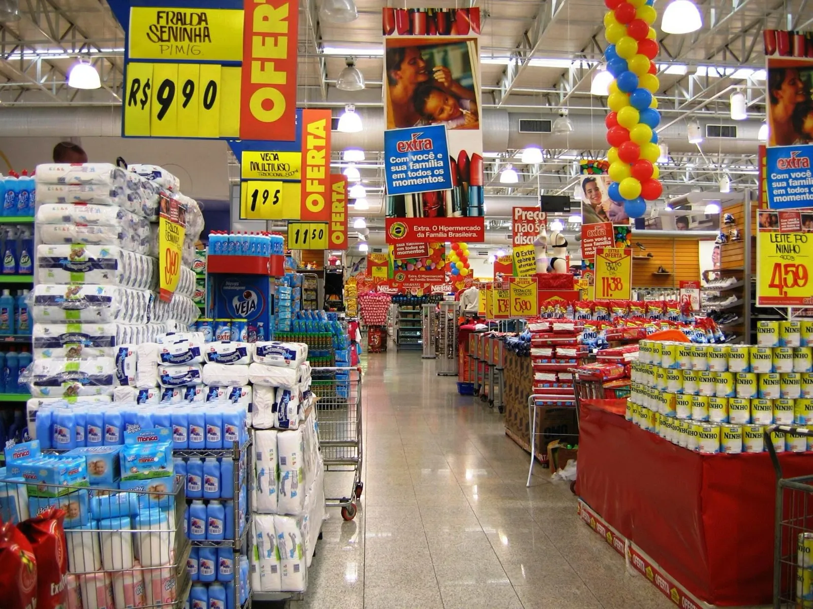 Corredor de supermercado com produtos de limpeza, alimentos e cartazes de preços