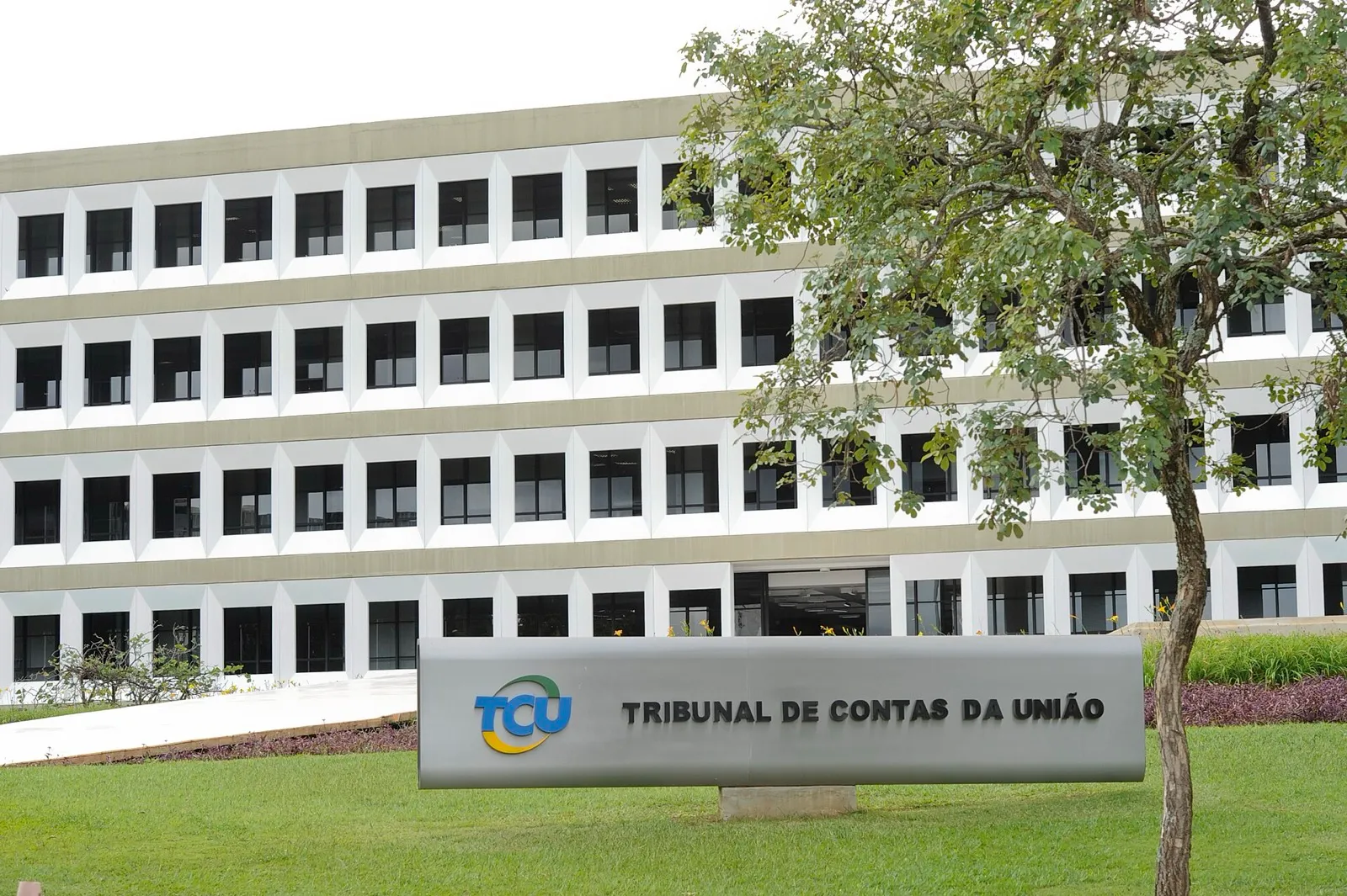 Prédio do Tribunal de Contas da União visto do jardim, com logotipo e nome do órgão